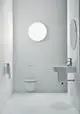 Weiße Badezimmerausstattung mit Waschtisch, Waschbecken und Toilette. Ideal Standard. Helle Wände und minimalistische Gestaltung. Runde Wandspiegel und Lichtquelle.